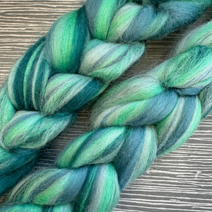 Braided skein of green and blue yarn on a wooden surface